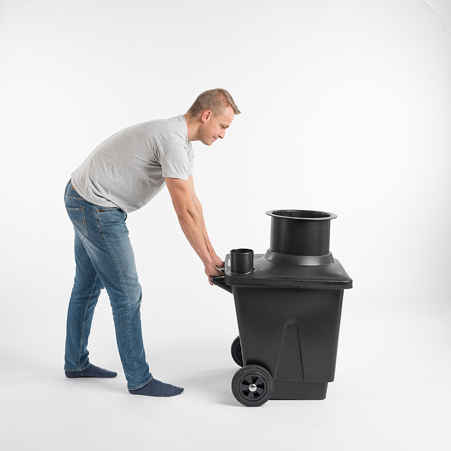 A man tilting a wheeled black composting container by its handle to move it